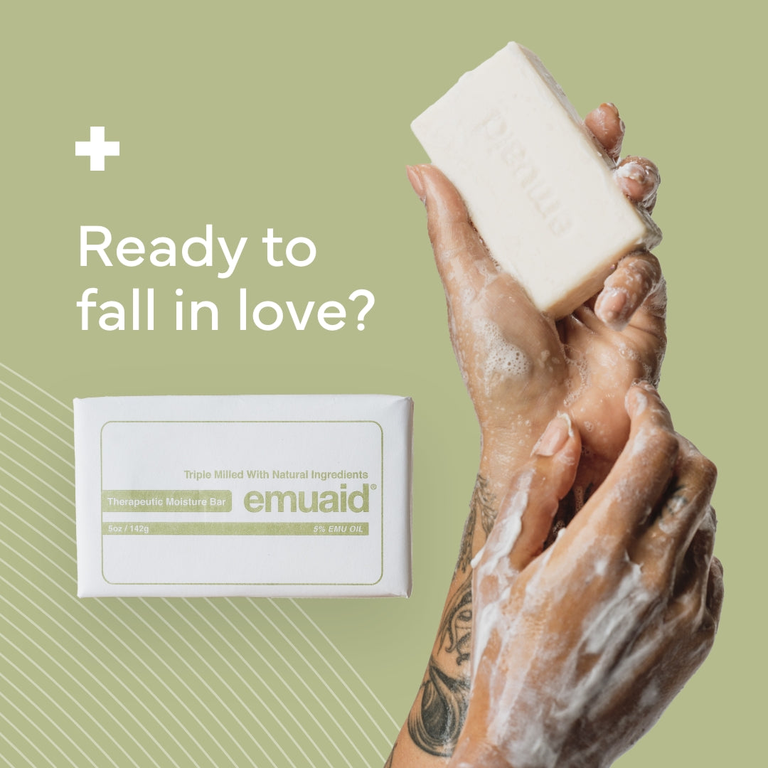 Hand holding a bar of soap with emuaid packaging on a green background