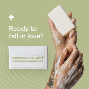 Hand holding a bar of soap with emuaid packaging on a green background