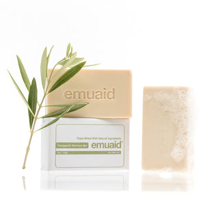 Emuaid soap bar with packaging and a green leaf on a white background