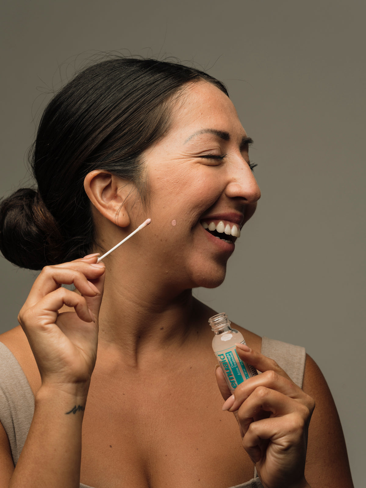 Donna che si applica un trattamento contro l'acne sul viso con un batuffolo di cotone su uno sfondo neutro